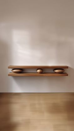 a shelf with three bowls on it in front of a white wall and wooden floor