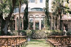 rows of wooden chairs sitting in front of a large building with trees and flowers on the lawn