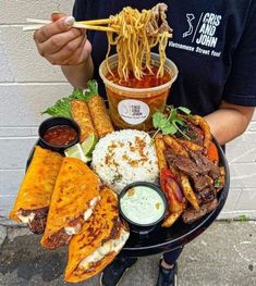 a person holding a plate with food on it and dipping sauces in the bowl