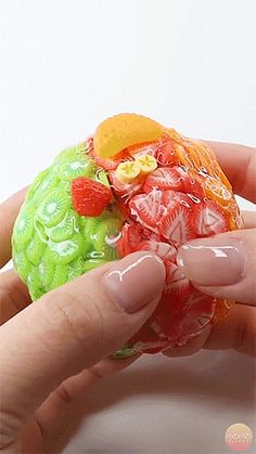 a hand is holding a small plastic ball with gummy bears on it's side