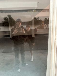 two people standing in front of a window taking a selfie with their cell phone