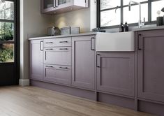 a kitchen with wooden flooring and gray cabinetry next to a large open window