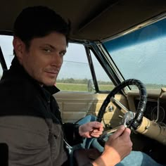 a man sitting in the driver's seat of a car holding a steering wheel