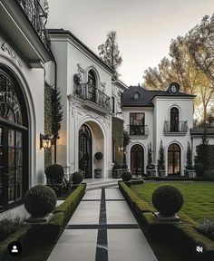 a large white house with lots of windows and bushes in front of it on a cloudy day