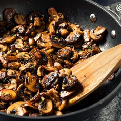 mushrooms are being cooked in a skillet with a wooden spoon