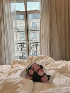 a bouquet of flowers sitting on top of a bed in front of an open window