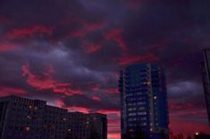 the sky is red and purple as it sets behind some tall buildings at night time