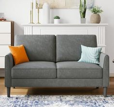 a gray couch sitting on top of a wooden floor next to a white dresser and potted plant