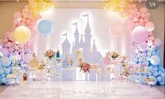 a table topped with lots of balloons next to a castle and castle cake stand on top of a white floor