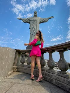 a woman in a pink dress standing next to a statue with her hand on her hip