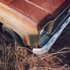 an old rusted out truck sitting in the middle of some dry grass and weeds