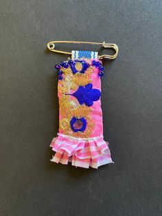 a pink and blue purse hanging from a hook on a black surface with other items in the background