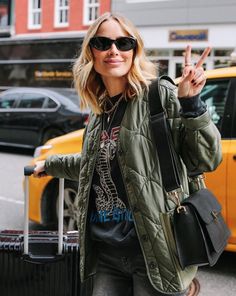 a woman is holding her hand up in the air while walking down the street with luggage