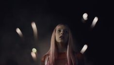 a woman with long pink hair standing in the dark, looking up at fireworks behind her