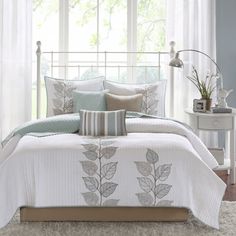 a bed with white and blue comforters in front of a window filled with curtains