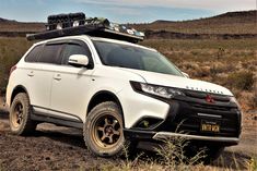 a white suv parked on the side of a dirt road with luggage strapped to it's roof