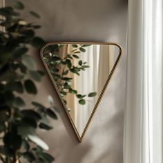 a triangle shaped mirror hanging on the wall next to a potted plant and window