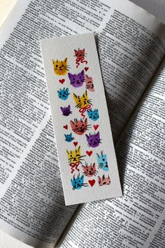 a bookmark with colorful cats on it sitting on top of an open book,