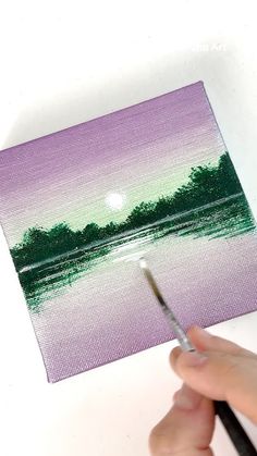 someone is holding a paintbrush and painting a landscape with purple, green and white colors