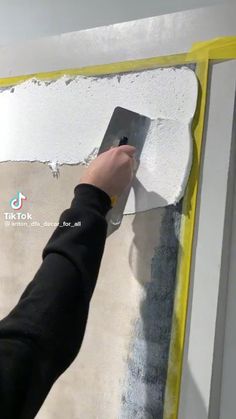 a person is using a paint roller to paint a wall with white and yellow stripes