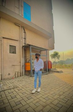 a man standing in front of a building with his hands in his pockets and sunglasses on