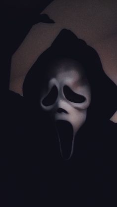 a person wearing a white mask with their mouth open and tongue out in the dark