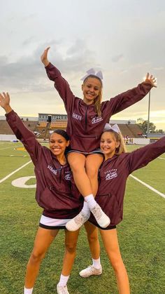 three girls are posing on the field with their arms in the air