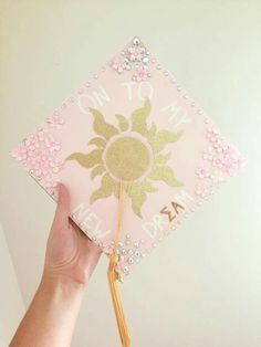 a hand holding a pink and gold graduation cap