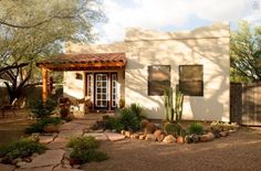 a small house with cactus and rocks in front of the door is surrounded by trees