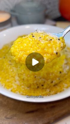 a spoon full of yellow food on top of a white bowl filled with rice and mustard