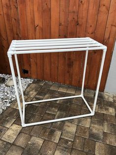 a white metal table sitting on top of a brick floor next to a wooden wall