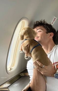 a man sitting on an airplane with his dog in his lap looking out the window