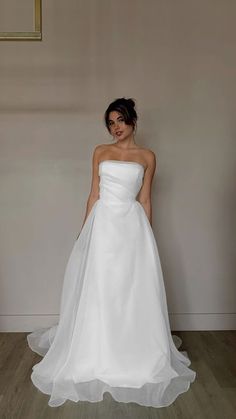 a woman in a white wedding dress standing next to a wall with a framed photo on it