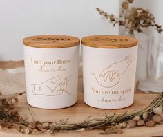 two white ceramic jars sitting on top of a wooden table next to some dried flowers