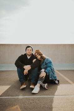 a man and woman sitting on the ground in an empty parking lot with their arms around each other