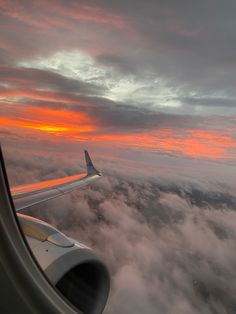 an airplane wing flying over the clouds at sunset