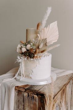 a white wedding cake with feathers and flowers on the top is sitting on a wooden table