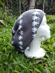 a white mannequin head wearing a gray and white knitted hat on top of green grass