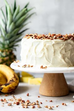 a cake with white frosting and walnuts on a plate next to two bananas