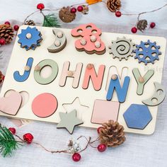 a wooden name board with christmas decorations and pine cones on the table next to it