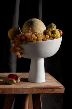 a white bowl filled with fruit sitting on top of a wooden table next to a black curtain