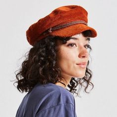 a woman with curly hair wearing an orange hat and looking off to the side while standing in front of a white background