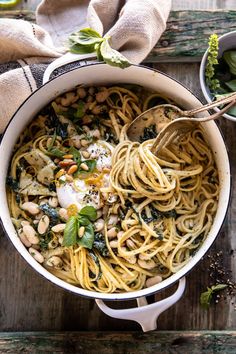 a pot filled with pasta, beans and spinach on top of a wooden table