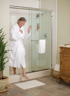 a woman in a white bathrobe standing on the edge of a shower door