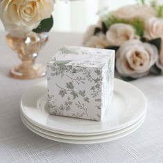 a white plate topped with a piece of cake next to a vase filled with flowers