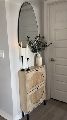 a white vase sitting on top of a wooden dresser next to a mirror and candles