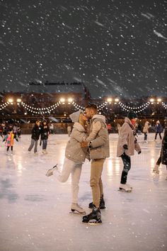 two people are skating on an ice rink at night with snow falling all around them