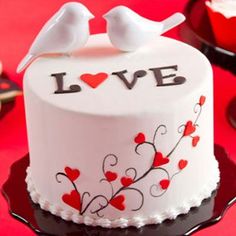 two white birds sitting on top of a cake decorated with red hearts and love letters