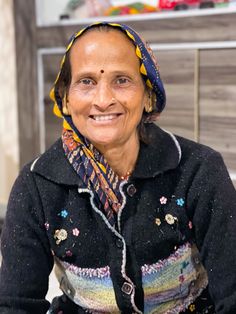 an old woman wearing a colorful head scarf and smiling at the camera while sitting down