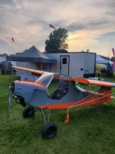 an orange and gray airplane parked on top of a lush green field next to tents